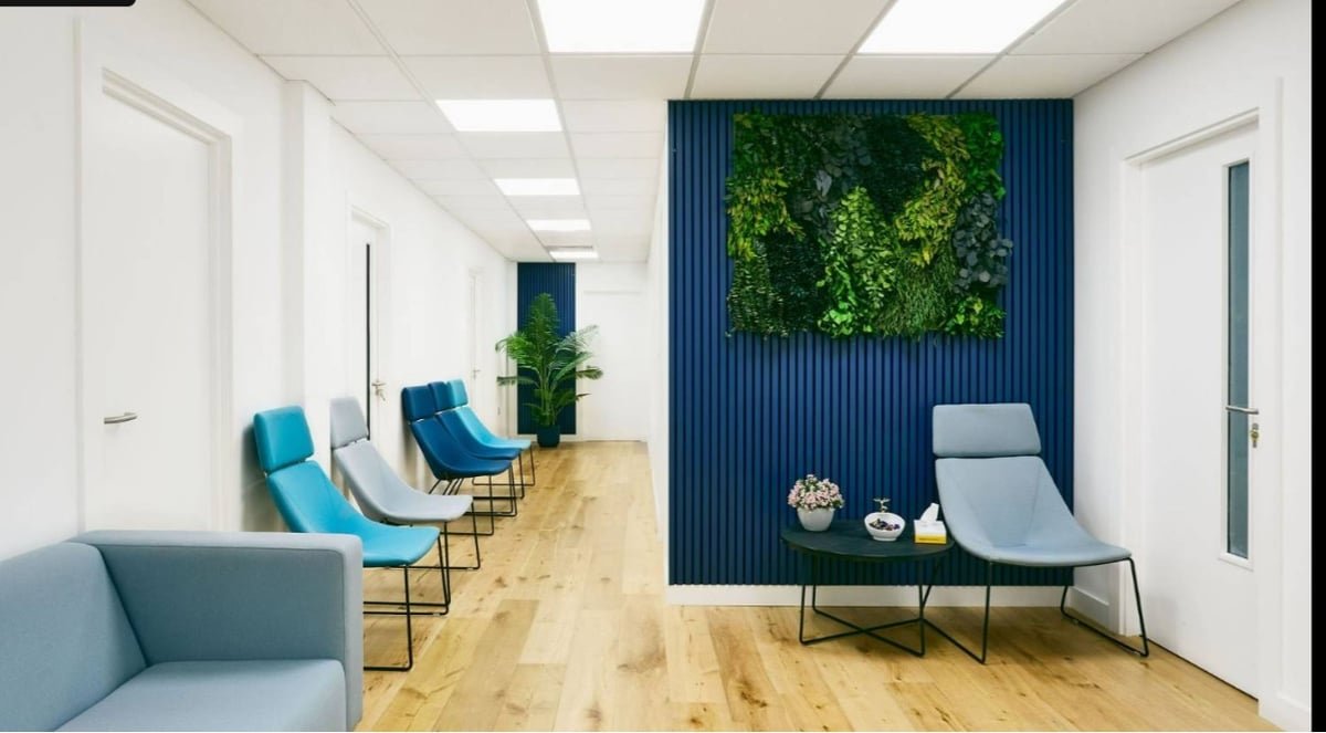 Modern waiting room of AristoGP clinic with blue and teal chairs, wooden flooring, and green wall decor, emphasizing a welcoming atmosphere for patients.